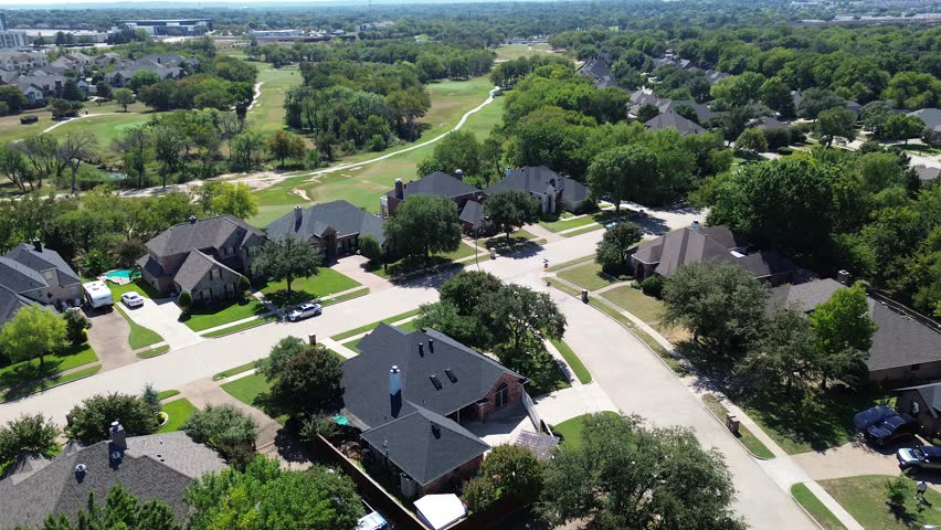 Upscale suburban houses with private pools adjacent to Iron Horse Golf Course in North Richland Hills, Texas. Curving streets, lush trees, and commercial rooftops frame horizon, suburbs Dallas. USA