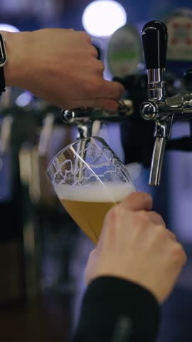 Bartender hands pour beer into a glass, slow motion vertical video