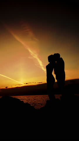 A silhouette of two people in love, a man and a woman, standing on the seashore at sunset. Family vacation on a tropical coast. Vertical video.