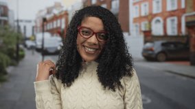 African american woman wearing bright red glasses smiles and touches hair on urban street; joy confidence. - Powered by Shutterstock - Get 15% off with code: PIKWIZARD15