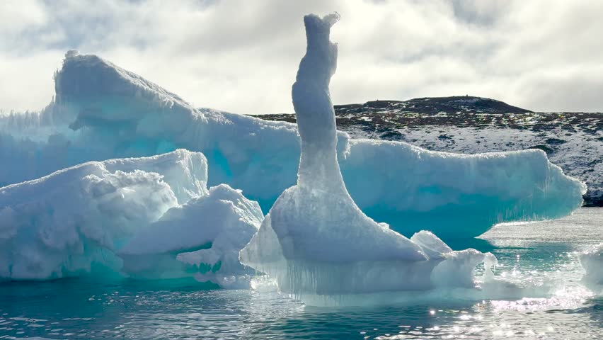 A striking ice formation towers over calm waters in a glacier lagoon, surrounded by stunning icy landscapes and mountainous terrain. The scene captures the beauty of Iceland