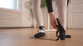 Ballerina puts on pointe shoes on leg in dance class. Classical ballet dancer woman in dance studio. Ballerina putting on tying classical pointe shoes for dance training. Ballet school concept - Powered by Shutterstock - Get 15% off with code: PIKWIZARD15