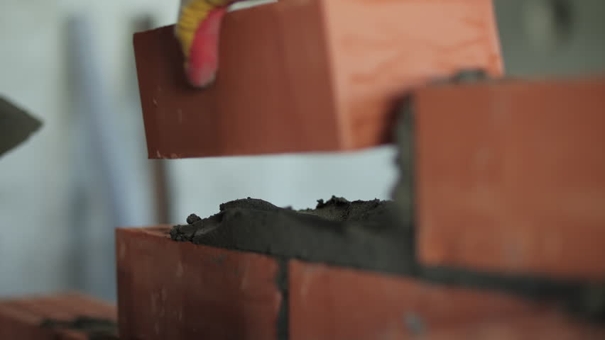 Bricklayer placing red clay bricks with mortar