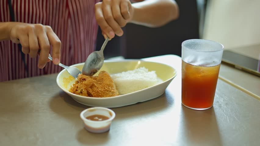 Woman in office enjoying quick lunch of fried chicken and rice, during quick lunch break with iced tea, her hand reaches for rice in quick lunch, great for corporate health work-life balance videos