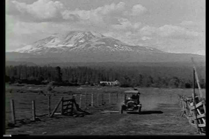 1900s - An old model T drives in front of a mountain range in California or Oregon.
