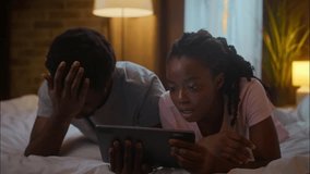 Displeased shocked African American family couple boyfriend man girlfriend woman lying bed use online digital tablet pad browsing internet lost connection failure problem error at home bedroom evening - Powered by Shutterstock - Get 15% off with code: PIKWIZARD15