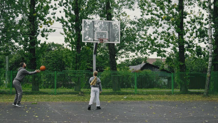 Little girl and her father throwing ball in basketball hoop outdoors. Young sportive father playing basketball with daughter. Father and daughter spend time together. Happy family time. 4K, UHD