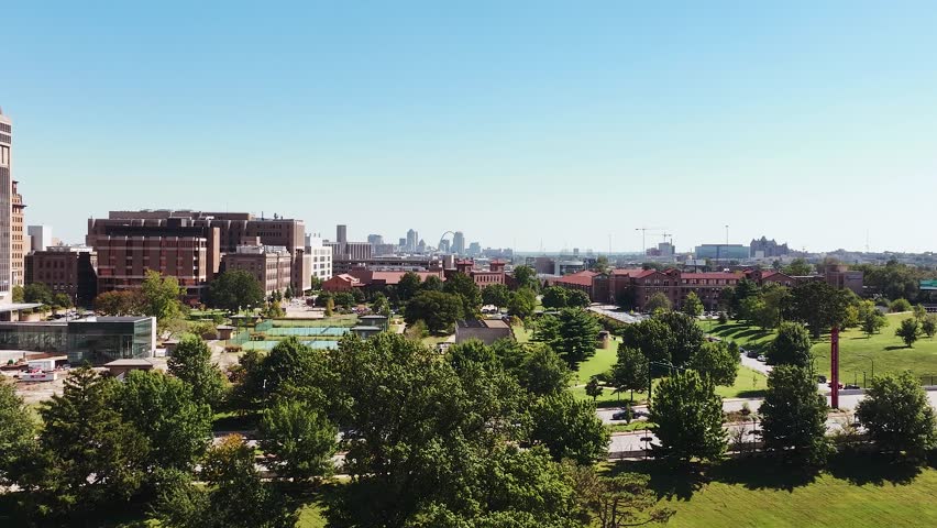 A cityscape view of downtown Saint Louis, Missouri with tall buildings, trees, and skyscrapers on a beautiful clear blue sky day