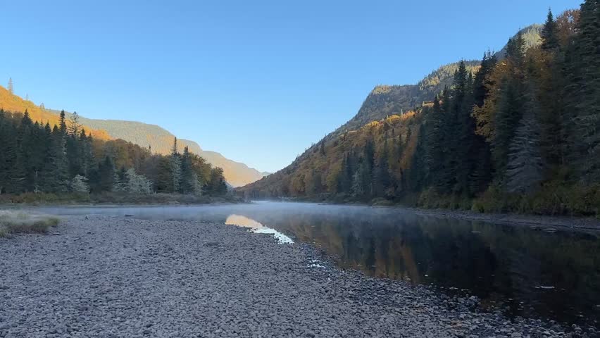 Video of an autumn lake at sunrise in Parc Jacques-Cartier, with mist rising from the cold water and golden foliage along the shore. Perfect for travel, tourism, and adventure content highlighting Can