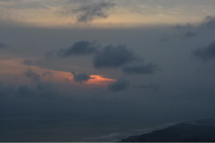Beautiful sunset over the ocean with dramatic dark clouds and soft orange light, creating a peaceful yet moody natural landscape background
