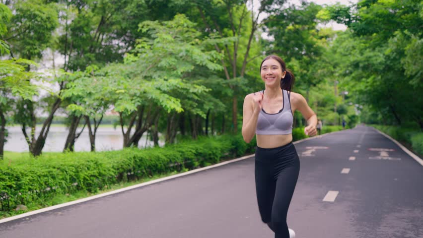Asian beautiful sportswoman doing running exercise alone in the garden. Attractive young athlete girl in sportswear feel happy and relax, enjoy practice workout for health care activity in public park