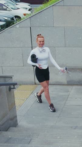 A Fit and Energetic Individual Enjoys a Post-Workout Stroll with Yoga Mat and Water Bottle, Radiating Confidence and Vitality in a Lively Urban Setting