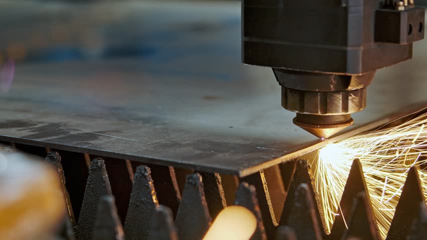 Industrial CNC laser cutting machine processing metal sheet with bright sparks and plasma light. High precision manufacturing technology in modern metalworking industry