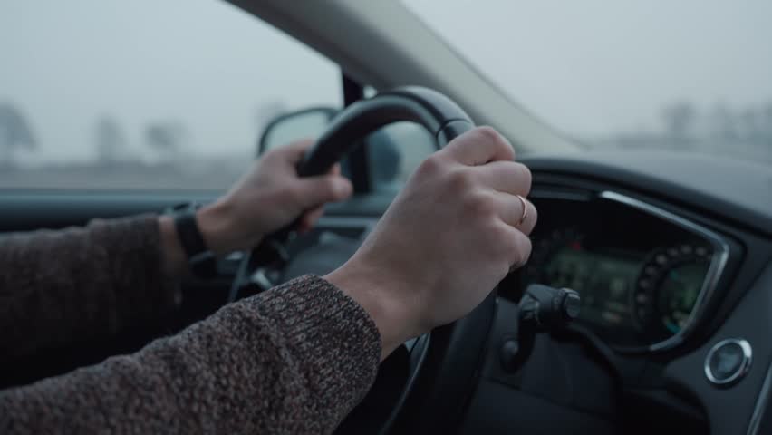 Close up of hands on steering wheel while driving car on foggy winter day. Travel, transportation and road safety concept