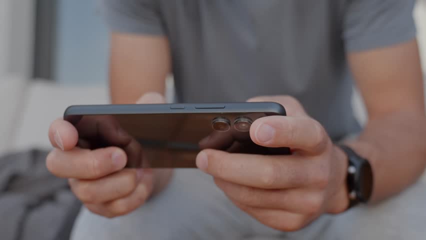 Man using smartphone, close up. Male hands holding smartphone and playing mobile game outdoors. Concept of technology, digital entertainment and gadget using