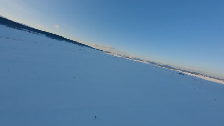 Aerial view of vast snow-covered mountain with clear blue sky, showcasing cold wilderness beauty.