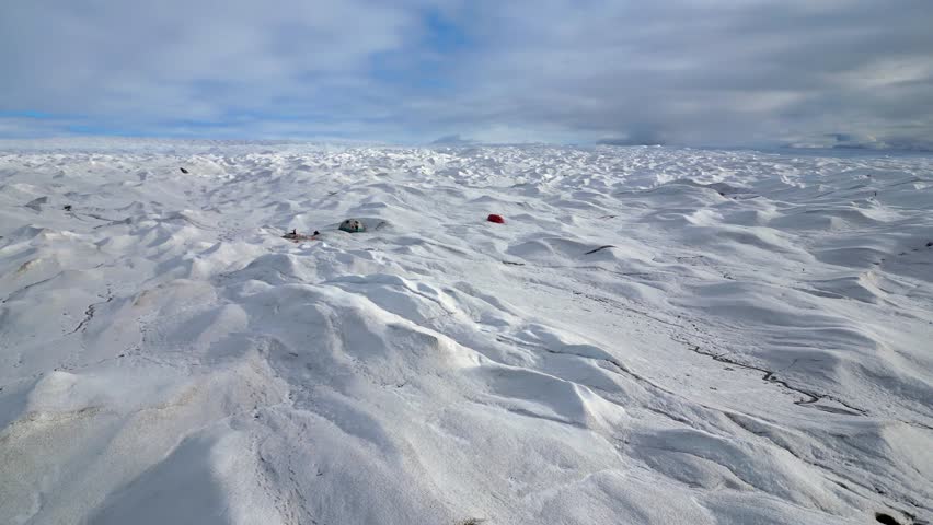 Low flyover of vast glacier toward tent camp set up for eco-tourism