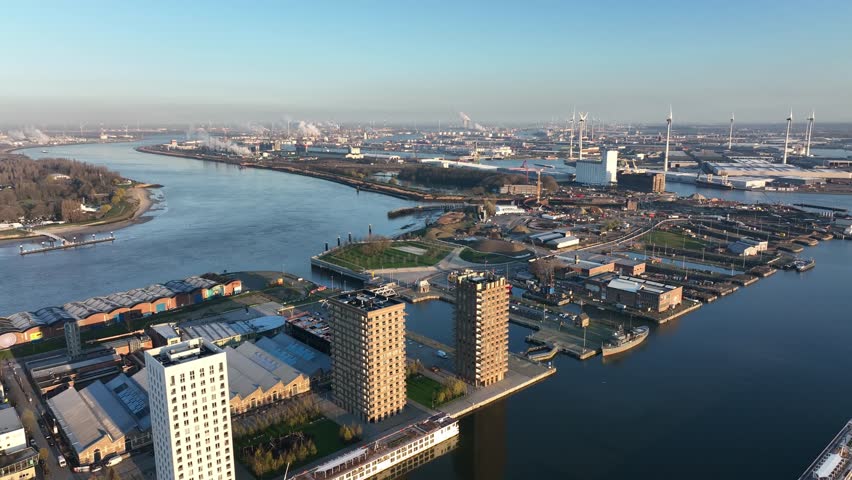 Semi orbit aerial shot of Antwerp harbor with high-rise towers, docks, warehouses, and industrial background under clear daylight