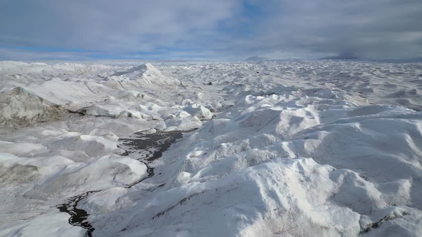 Low flyover of frozen lake on barren, sunny arctic Greenland glacier