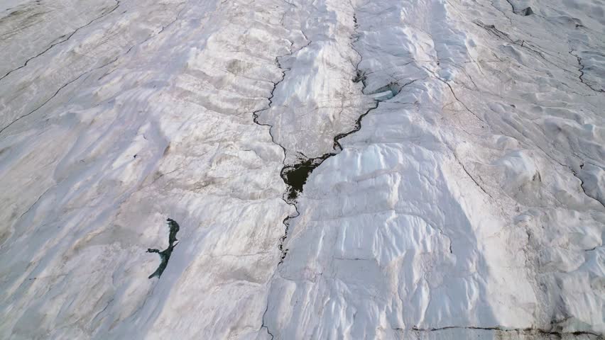Flyover dark river carved into textured surface of vast arctic glacier ice sheet