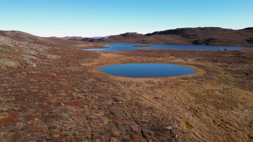 Flyover golden amber summer tundra lakes in barren Greenland arctic