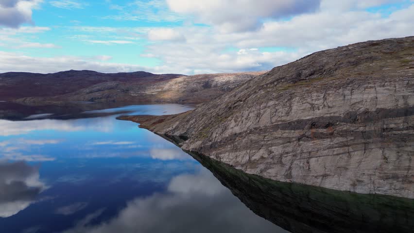 Angled bedrock bedding plane dips into reflective blue arctic lake