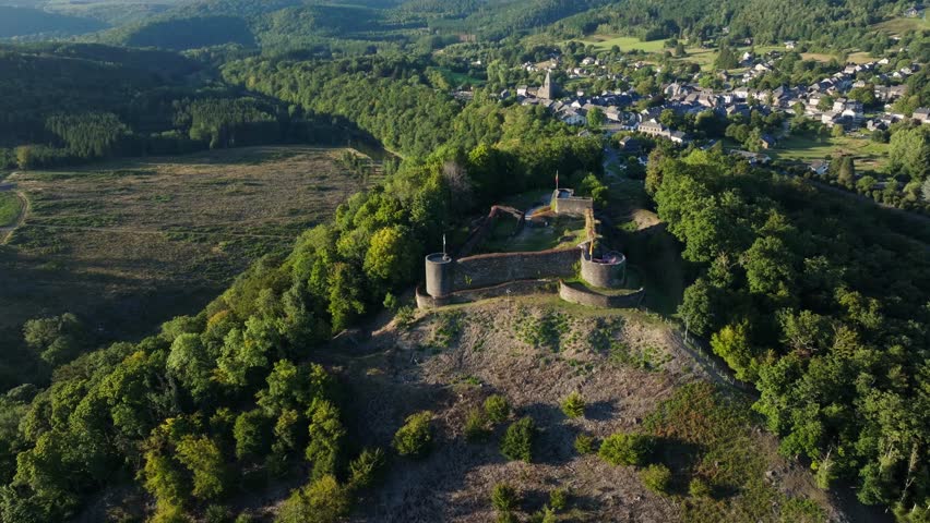 Aerial wide orbiting shot of the historic Herbeumont castle on a hill overlooking valley and city nearby