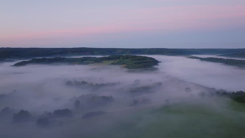 Morning mist by fields, forest and roads in the Ardennes, aerial push-in
