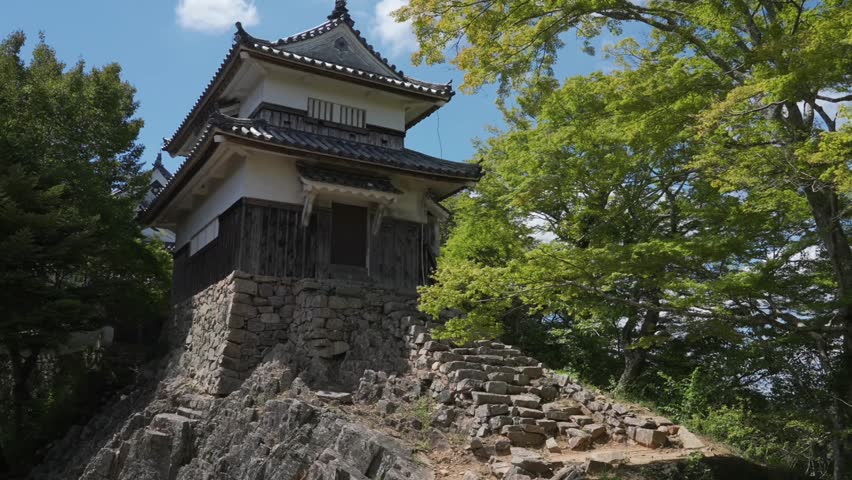 Bitchu Matsuyama Castle's two-story turret (Japan's Top 100 Castles): Ancient wooden pavilion-style structure on mountaintop rocks and stone walls, with lush trees and clear sky.
