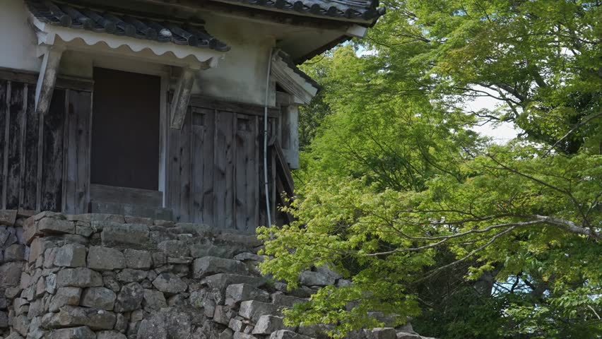 Bitchu Matsuyama Castle's two-story yagura (Japan's Top 100 Castles): Ancient wooden pavilion-style structure on mountaintop rocks and stone walls, with lush trees and blue sky.