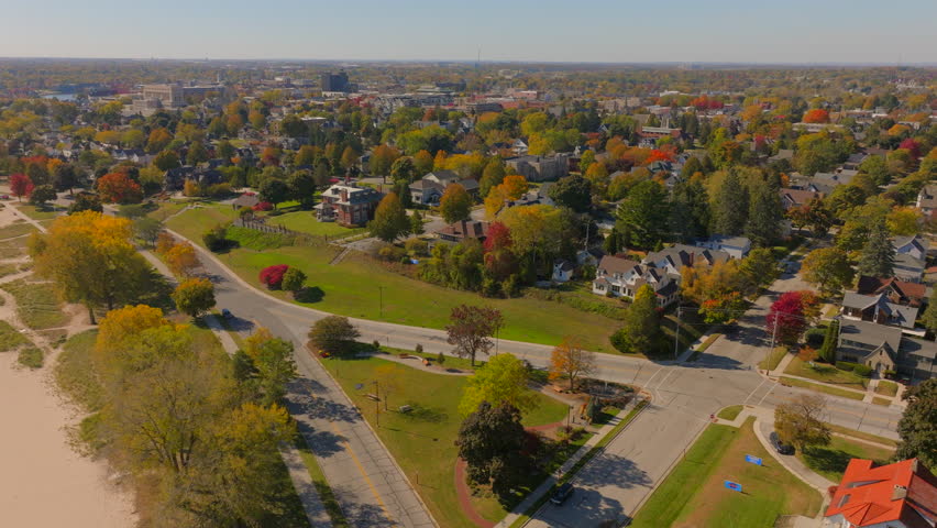 Drone aerial panning over Sheboygan, Wisconsin neighborhood with houses and trees at peak autumn color, revealing the beach and Lake Michigan on a gorgeous clear blue sky day.