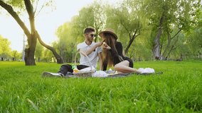 young couple in love sits on blanket on the grass and eats wine and croissants, man and woman relax on picnic in the park - Powered by Shutterstock - Get 15% off with code: PIKWIZARD15