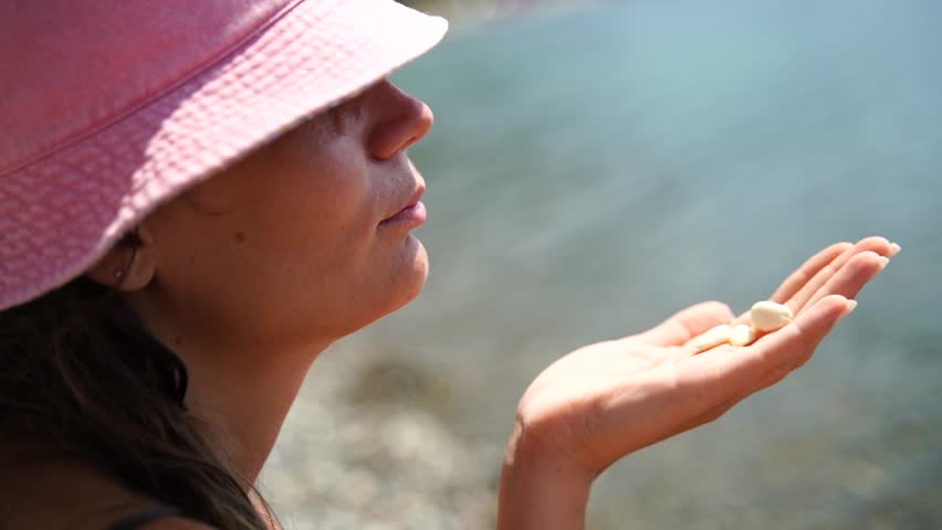 Woman Beach Sun: Lady holds shells on a sunny beach during daytime, perhaps appreciating nature.