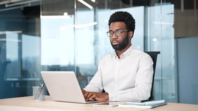 Portrait of serious african american businessman sitting at desk at workplace in modern glass business office. Confident successful proud manager working on laptop and looking at camera in workspace - Powered by Shutterstock - Get 15% off with code: PIKWIZARD15