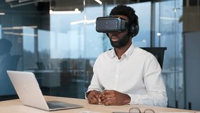 African american businessman using VR glasses for video call and online chat in virtual reality simulator sitting at workplace in office. Manager at a remote conference. Meeting with business partners - Powered by Shutterstock - Get 15% off with code: PIKWIZARD15