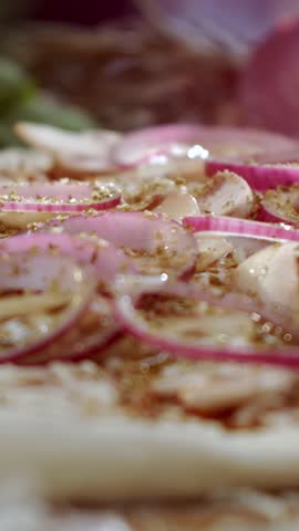 Close-up view of a chef pouring extra virgin olive oil over a raw homemade pizza with red onion, mushrooms, and cheese before baking, showcasing the preparation of italian cuisine