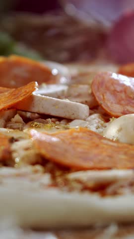 Delicious chopped bell peppers and spicy chili falling in slow motion onto an uncooked pepperoni pizza with mushrooms, part of a traditional italian food preparation process in a kitchen