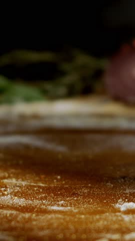 Freshly baked pizza topped with red onion and chili peppers resting on a wooden board while a chef sprinkles oregano over it. Fragrant steam rises from the hot, appetizing italian dish