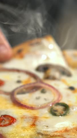 Hot, steaming slice of delicious italian pizza being lifted up, showing long strings of melted mozzarella cheese in an appetizing close-up view from a professional kitchen or restaurant