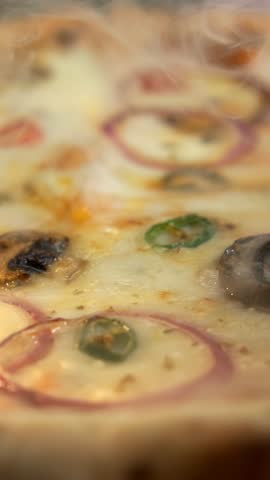 Delicious hot vegetarian pizza straight from the oven with mushrooms. Peppers. Onions. And melting mozzarella cheese. The appetizing steam rises from the freshly baked italian food on a wooden board