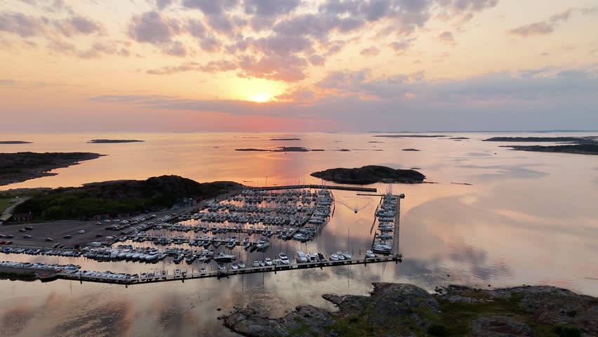 Enjoy the serene beauty of boats resting in a harbor during sunset in Sweden. The calm waters reflect the colorful sky as the sun sets over the horizon, creating a peaceful atmosphere.