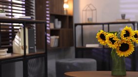 Beautiful sunflowers in vase on wooden table indoors, selective focus. Woman reading magazine on sofa, camera moving right - Powered by Shutterstock - Get 15% off with code: PIKWIZARD15