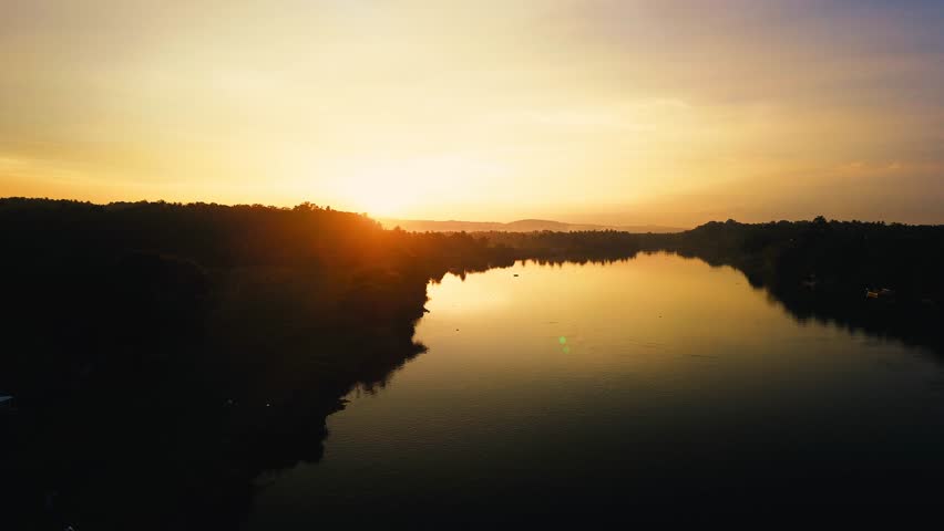 Cinematic drone footage of a majestic river flowing under glowing sunset sky.