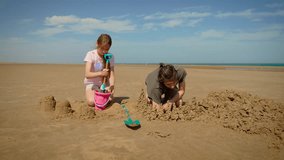 Kids building sandcastles with bucket and shovels, enjoying creative play. Teenagers shaping sandy towers together, smiling on sunny beach. Boy and girl constructing fun sand structures, working - Powered by Shutterstock - Get 15% off with code: PIKWIZARD15