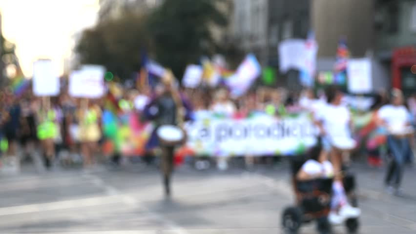 Colorful public pride parade with diverse crowd marching on city street carrying banners and rainbow flags, celebrating LGBT community, human rights, freedom, diversity and equality