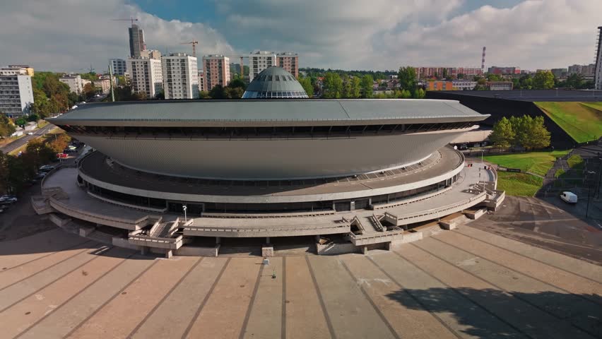Katowice, Poland - 09 October 2025: Aerial view of the iconic Spodek Arena juxtaposed against modern buildings and green spaces, a blend of architectural styles.