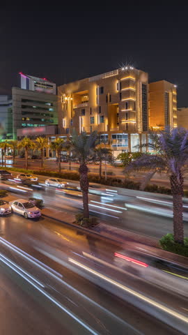 Cityscape aerial night timelapse of Riyadh, Saudi Arabia, featuring illuminated famous towers, skyscrapers, King Fahd Road and busy traffic. Palms and streetlights line the main highway through a city