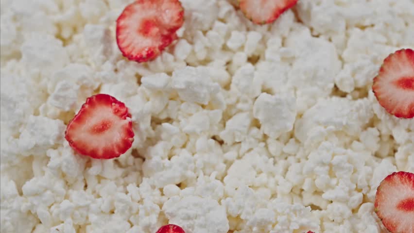 Close-up of fresh cottage cheese topped with a spoonful of sour cream, sliced strawberries. Healthy breakfast or dessert made with dairy protein, seasonal fruit. Probiotic cold fermented kefir, yogurt