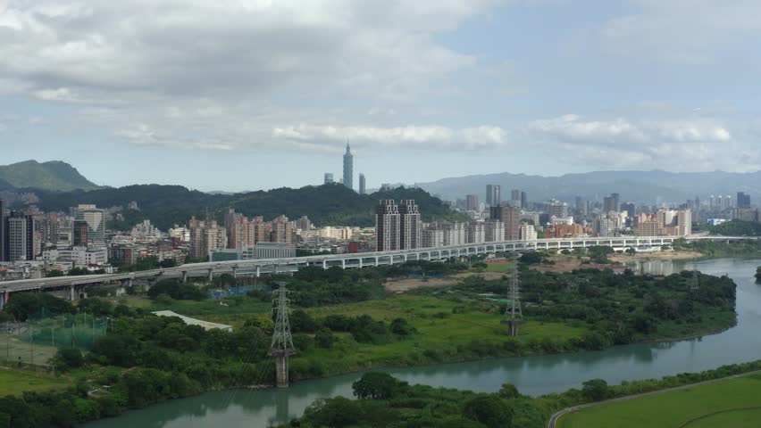 4K drone aerial shot slowly zooming out to reveal park landscape, river stream, and Taipei 101 building in the distance, with city transportation.