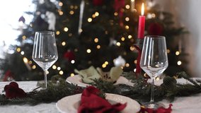 Stylish christmas table setting. Festive napkin on plate, cutlery, fir branches and berries,glasses and candle on rustic table against christmas tree twinkling lights. Serving xmas dinner video - Powered by Shutterstock - Get 15% off with code: PIKWIZARD15